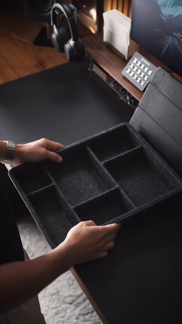 Grey felt desk organizer with compartments held by hands over a black desk mat