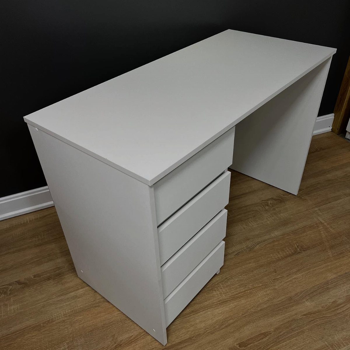 White minimalist desk with three drawers on a light brown wooden floor.