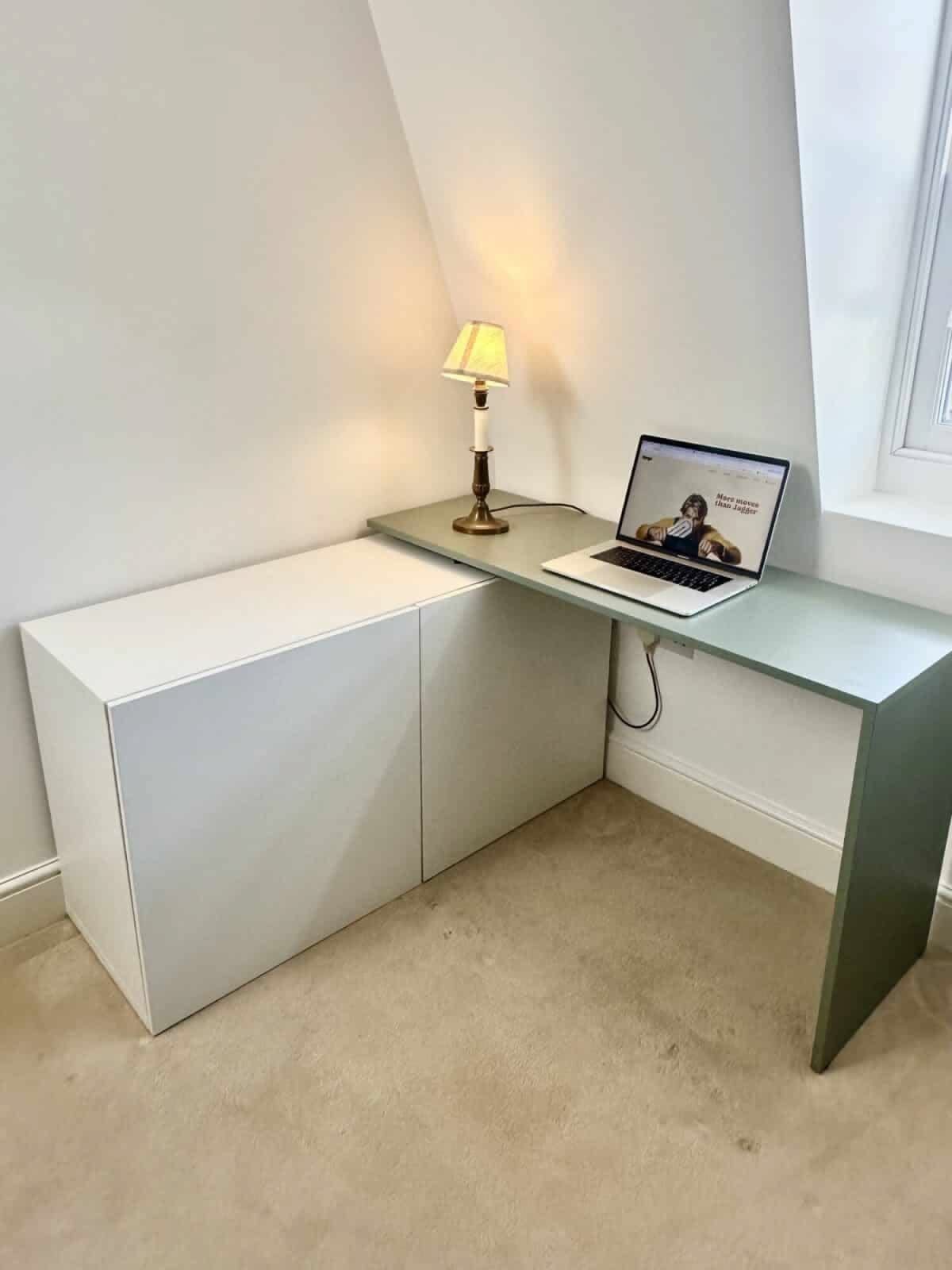 L-shaped white and green desk with laptop and lamp in a small corner