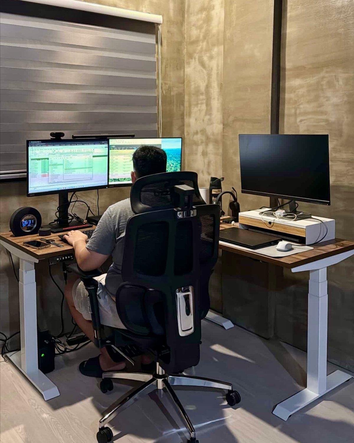 Person sitting in an ergonomic chair at an L-shaped desk with three monitors.