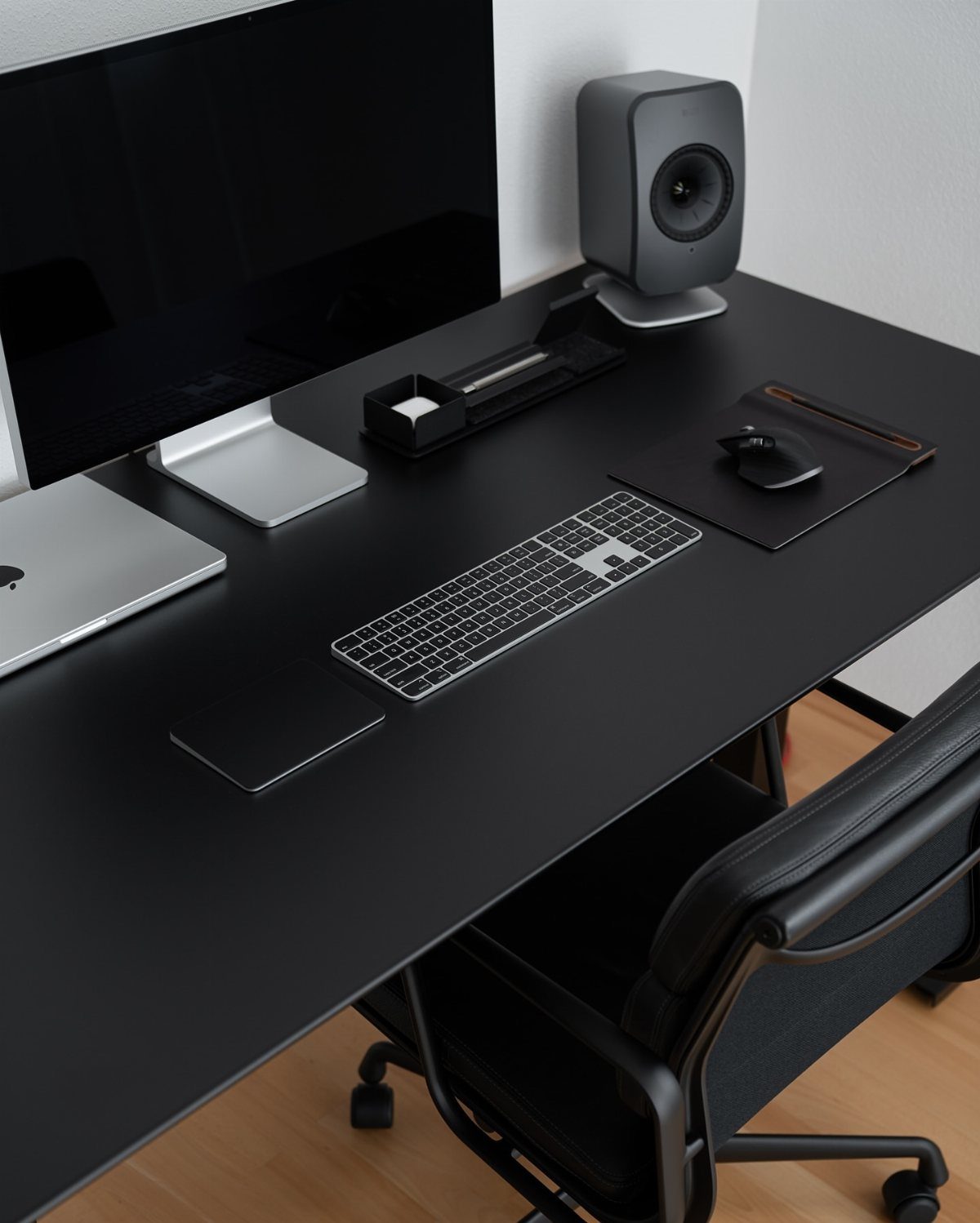 Minimalist black desk setup with laptop, monitor, wireless keyboard, and office chair.