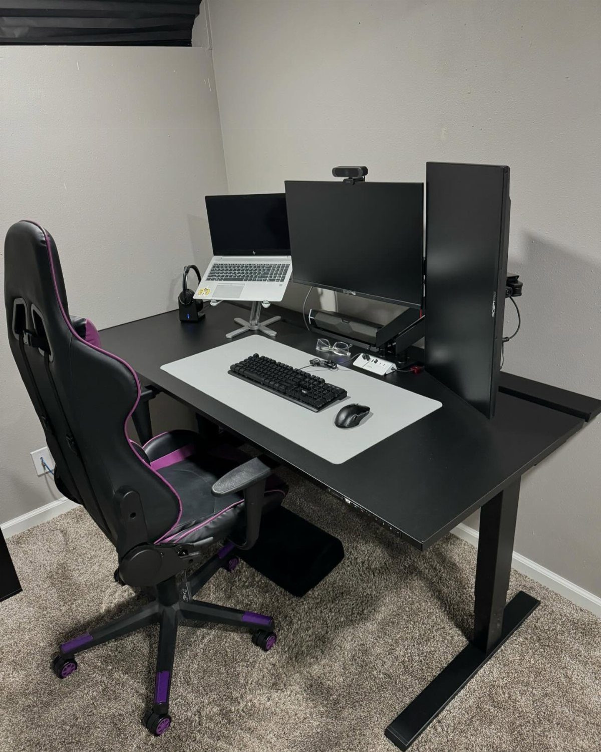 Desk setup with laptop on stand, two monitors, and a gaming chair.