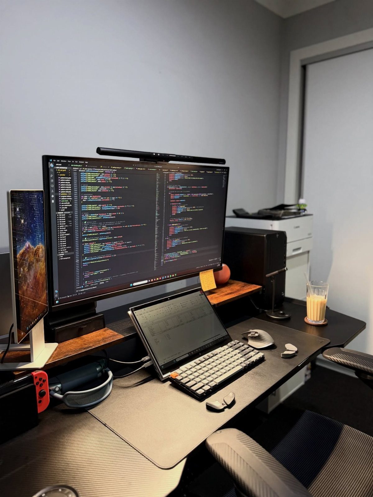 Large computer monitor displaying code positioned at eye level above a laptop and keyboard