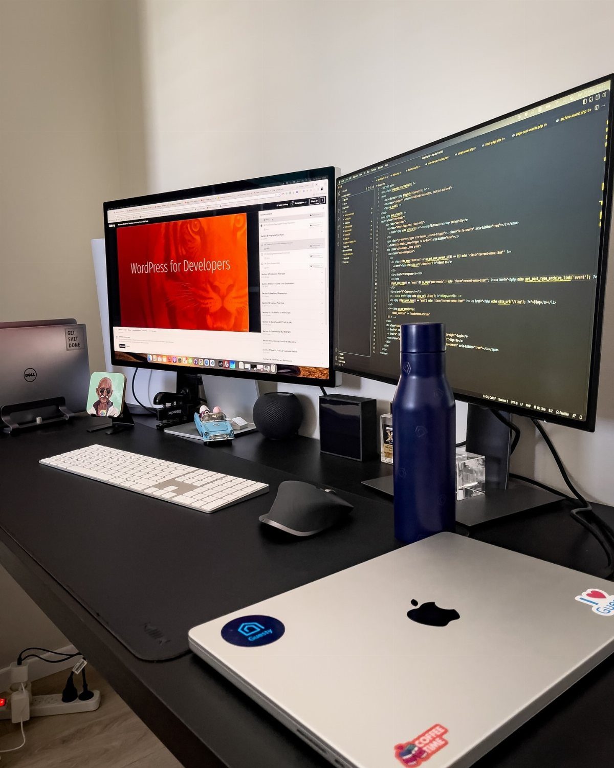 Two computer monitors and a laptop on a black desk with peripherals.