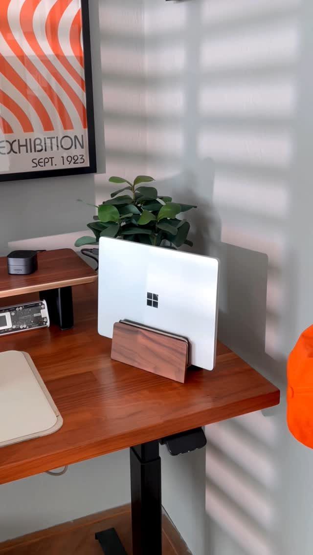 Silver laptop held upright by a wooden vertical stand on a wooden desk