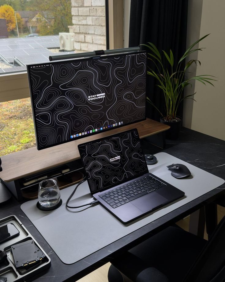 Laptop and monitor desk setup with matching wallpapers, grey mat, and potted plant.