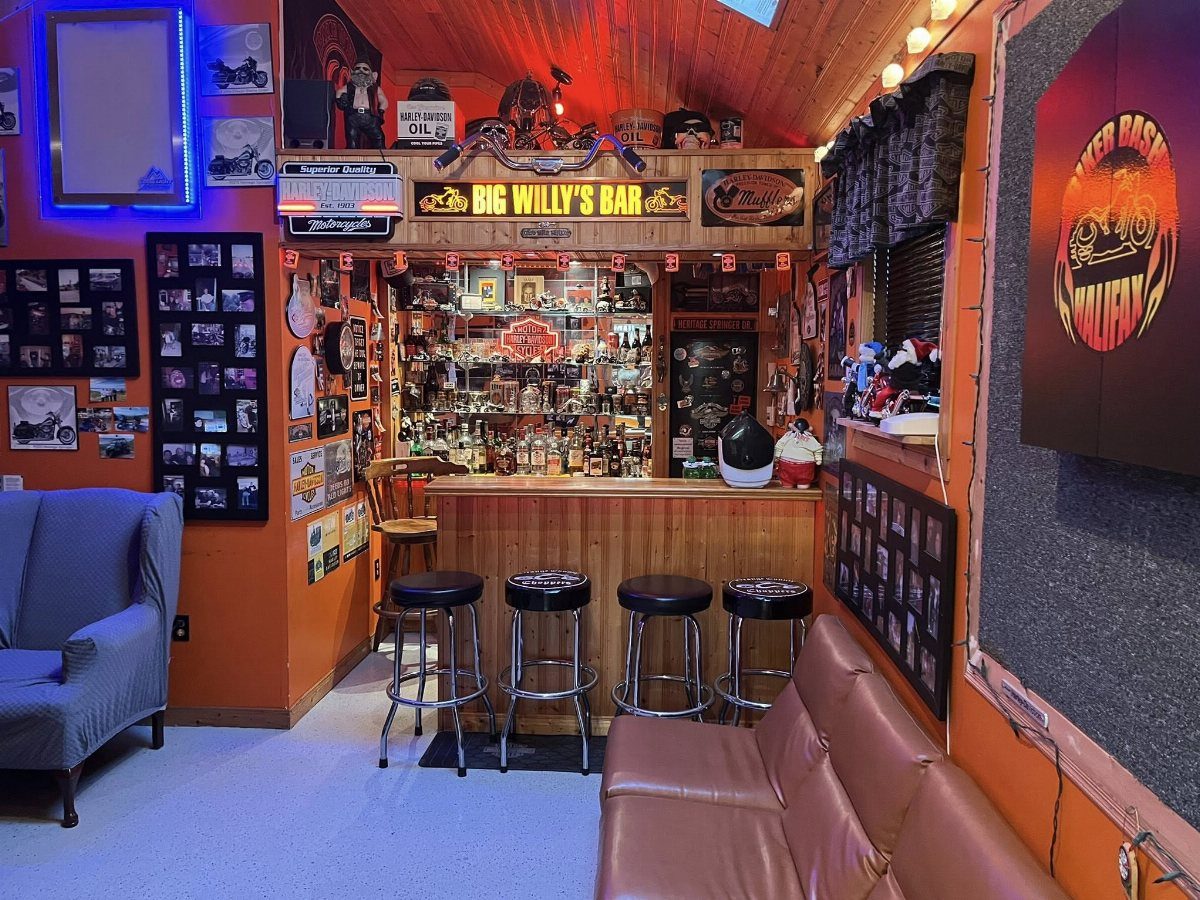 Home bar with wooden counter, black stools, orange walls, and various memorabilia decorations.
