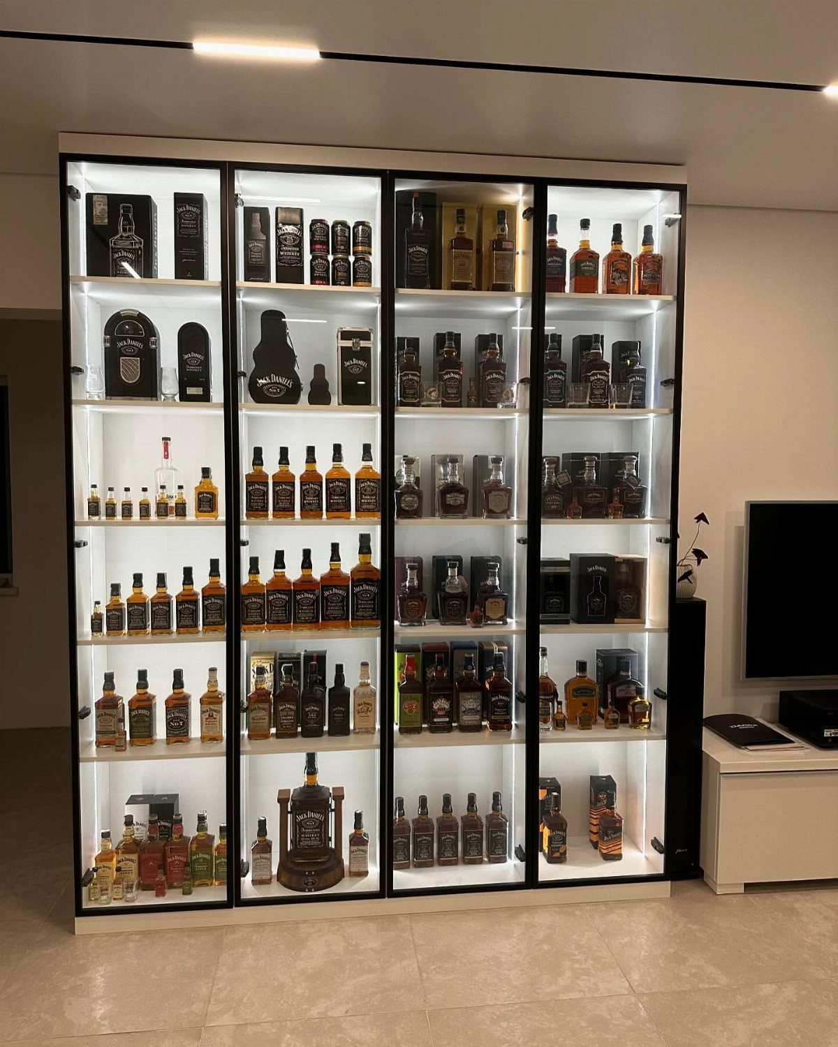 Lit glass display cabinet filled with various liquor bottles against a white wall