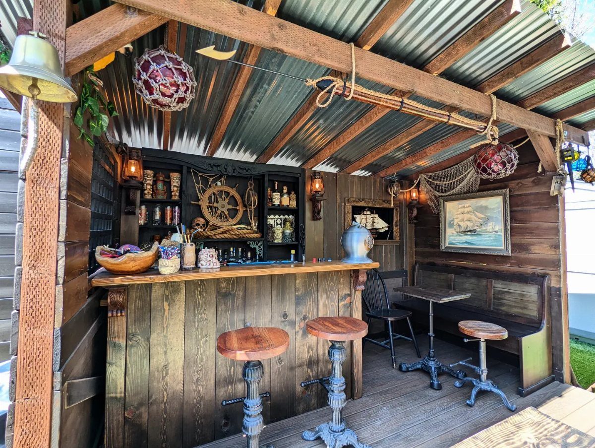 Nautical themed outdoor wooden bar with ship's wheel, fishing nets, and brass bell.