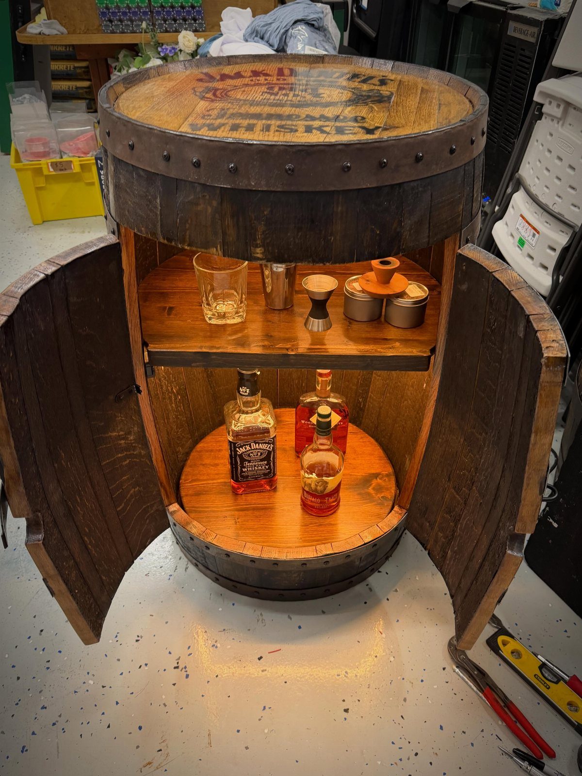 Whiskey barrel bar station with open doors revealing liquor bottles and bar tools