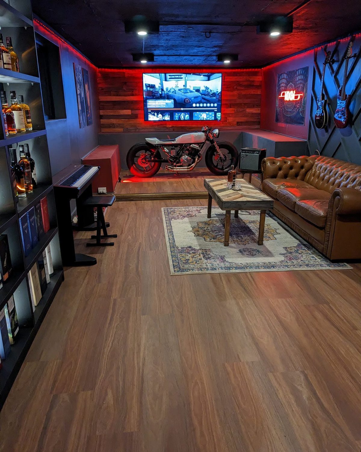 Man cave interior with red ambient LED lighting, leather sofa, and motorcycle display.