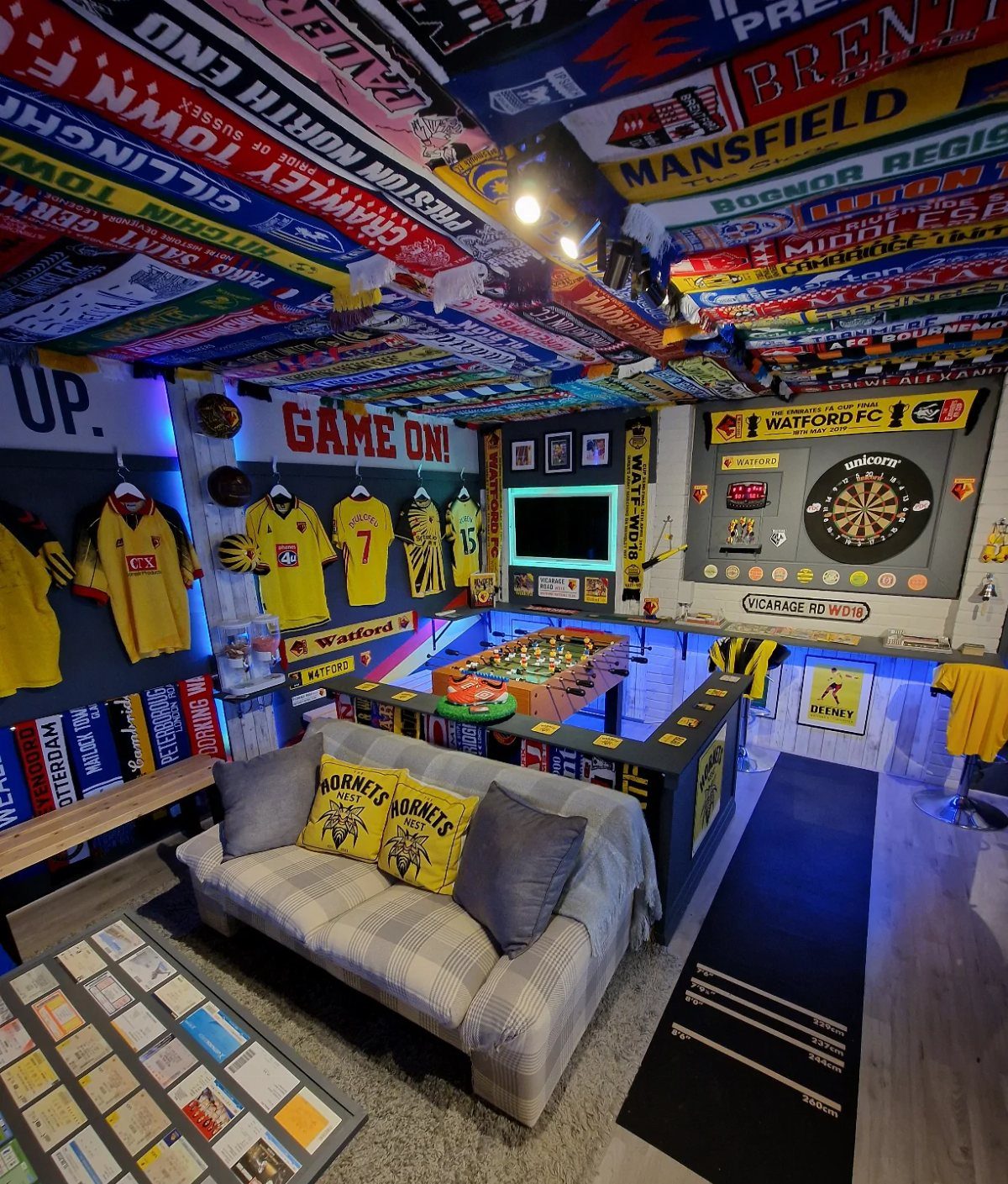 Sports-themed man cave with a dartboard, foosball table, and scarves on the ceiling.
