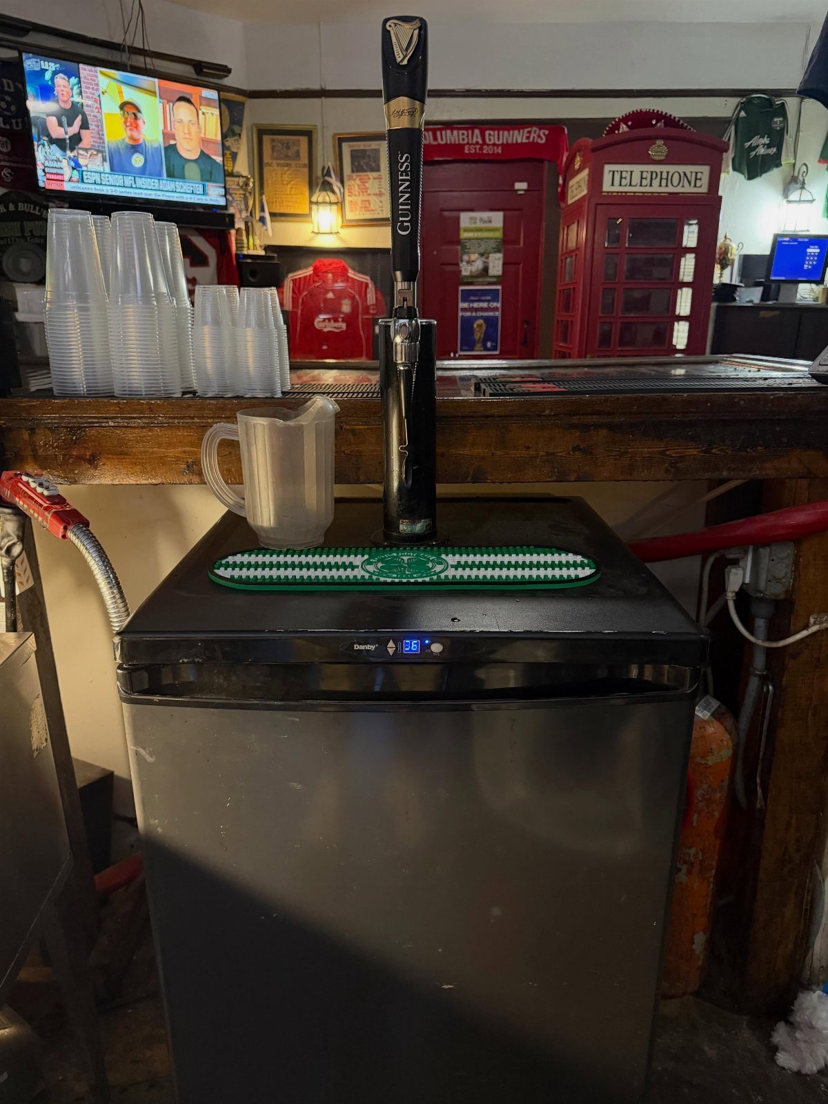 Stainless steel kegerator with a Guinness tap handle under a wooden bar counter.
