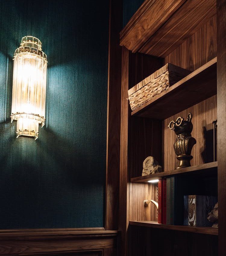 Wooden bookshelf with decorative items next to a glowing glass wall sconce.