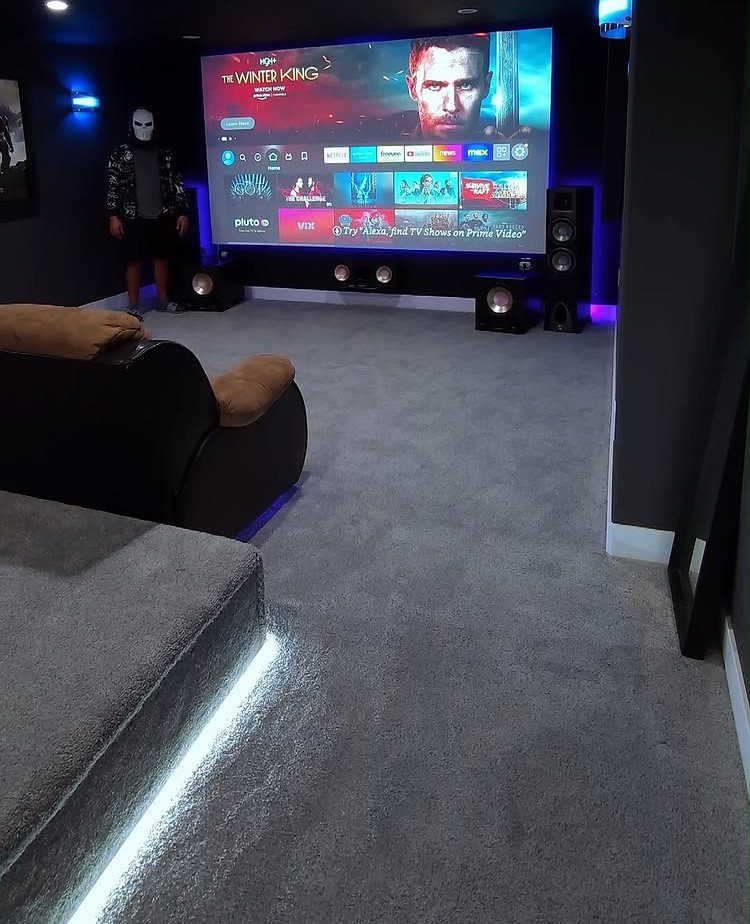 Home cinema room with a large projection screen, leather recliners, and blue LED lighting.