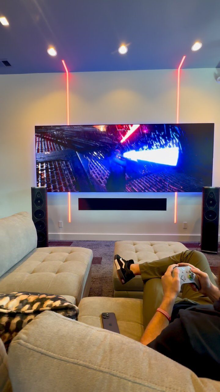 Wall-mounted television in a modern man cave with red LED lighting and speakers.