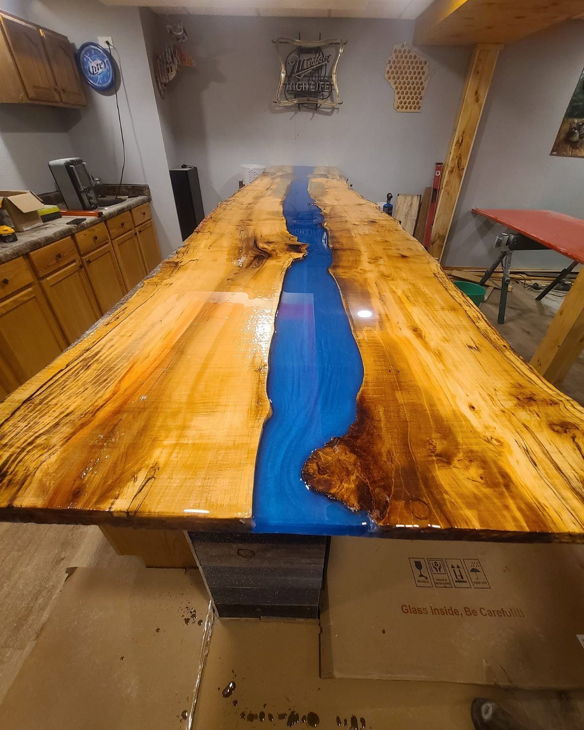 Live-edge wooden table with a blue epoxy resin river in a basement setting.