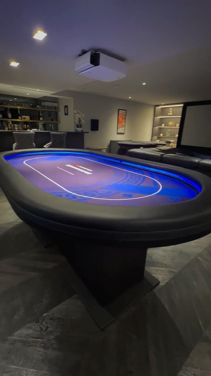 Oval poker table with blue glowing surface in a modern man cave basement