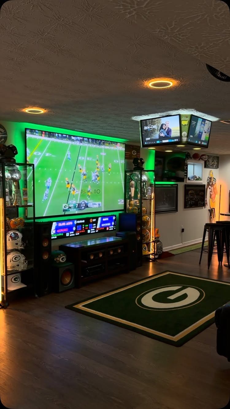 Sports themed man cave with large screen, memorabilia displays, and Packers area rug.