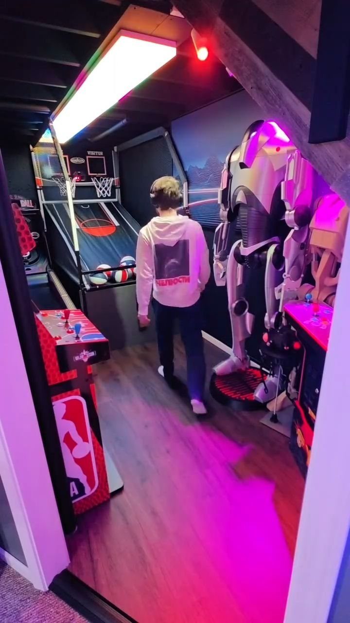 Man standing in a gaming room with arcade basketball and purple neon lighting.