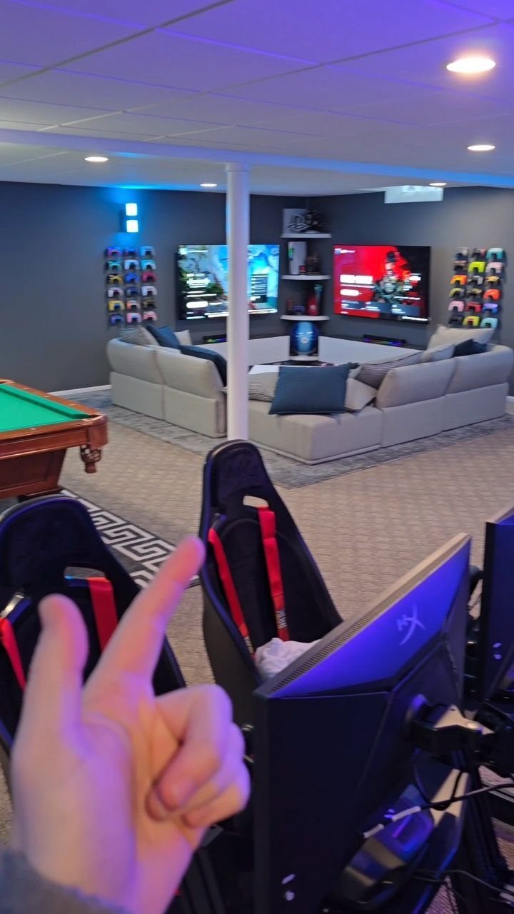 Basement game room with blue lighting, gaming chairs, pool table, and large sectional sofa.
