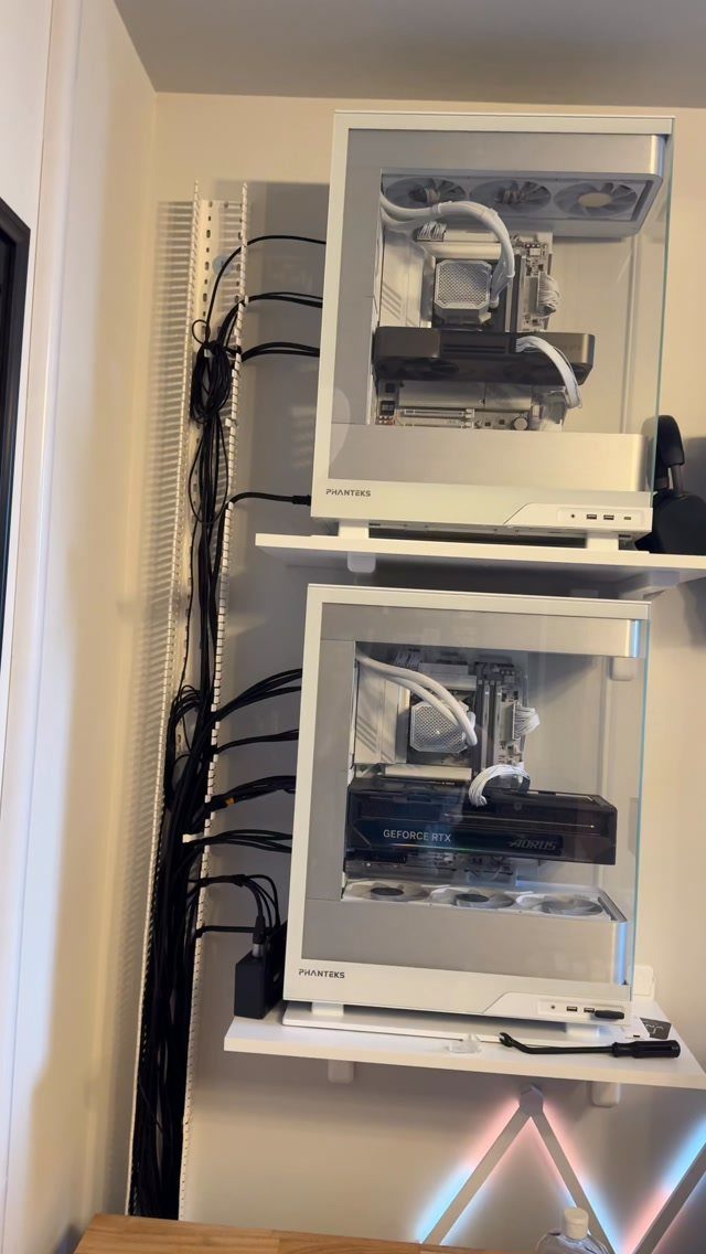 Two white gaming PCs on shelves with cables organized in a wall tray.