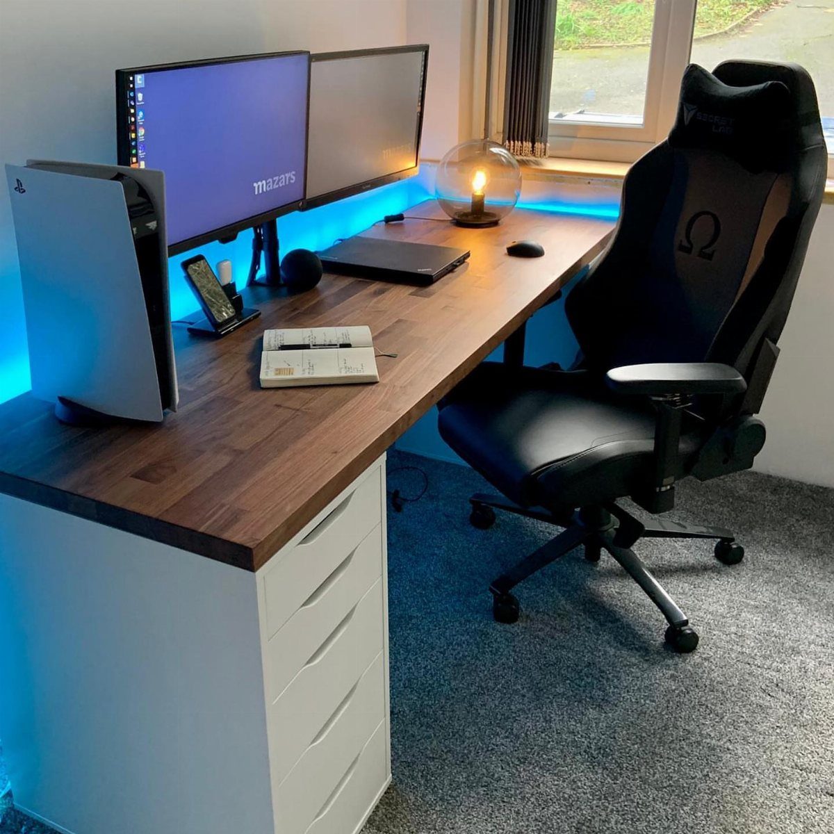 Gaming setup with wooden desk, dual monitors, PS5, and black gaming chair.