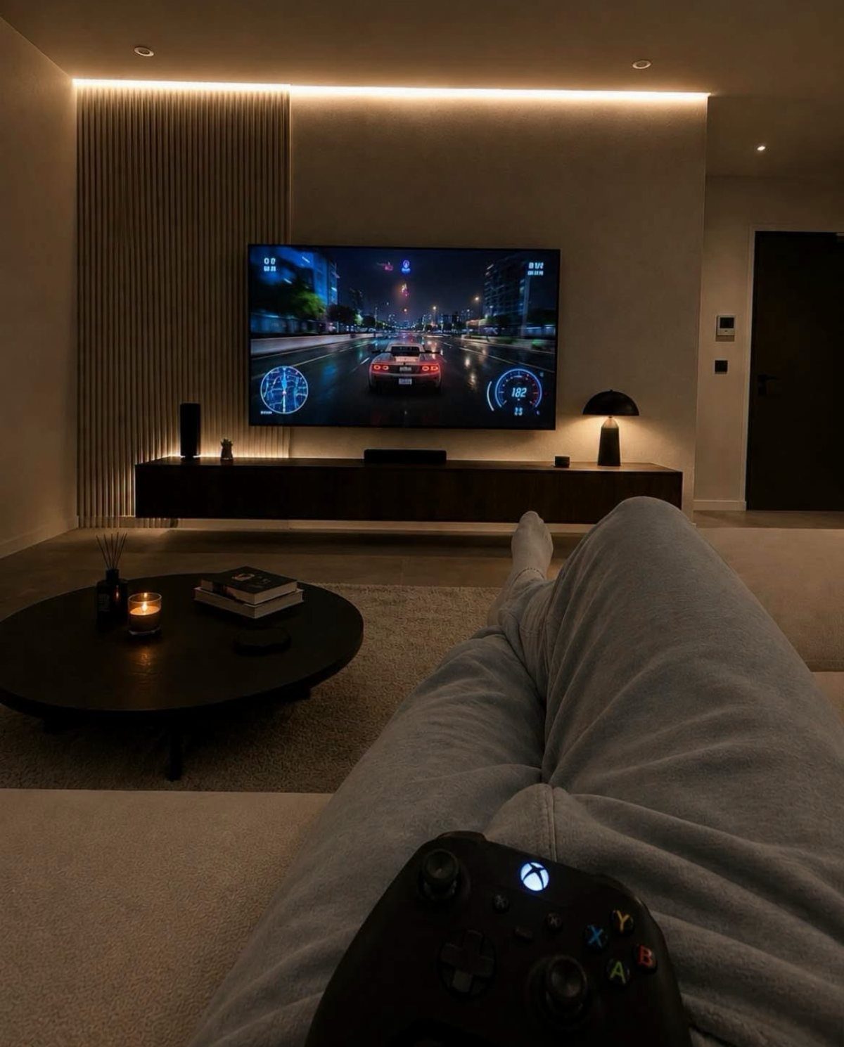 Person relaxing on a sofa with a controller facing a minimalist gaming setup.