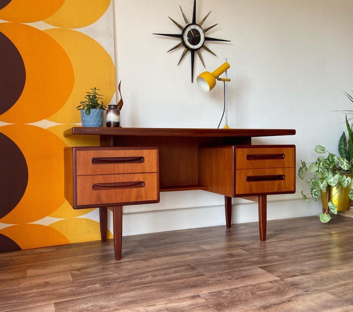 Mid century modern wooden desk with tapered legs and a yellow desk lamp.