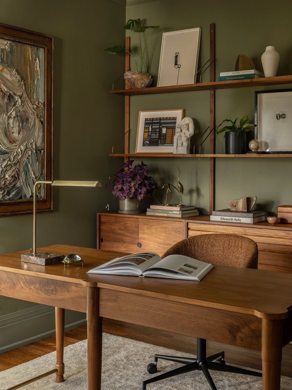 Wooden mid century modern desk and shelving unit against olive green walls