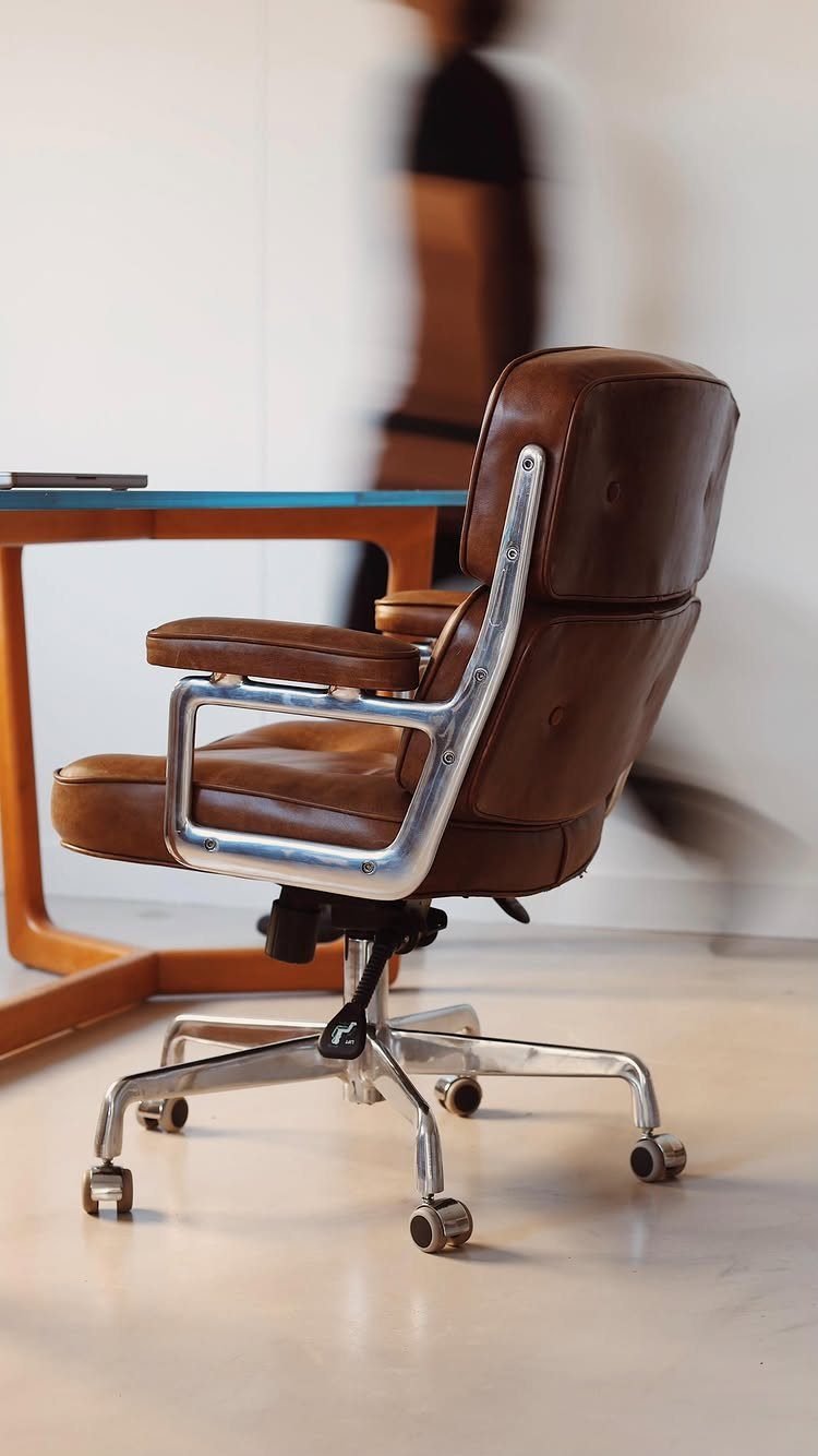Brown leather mid-century modern office chair next to a blue desk in a bright room
