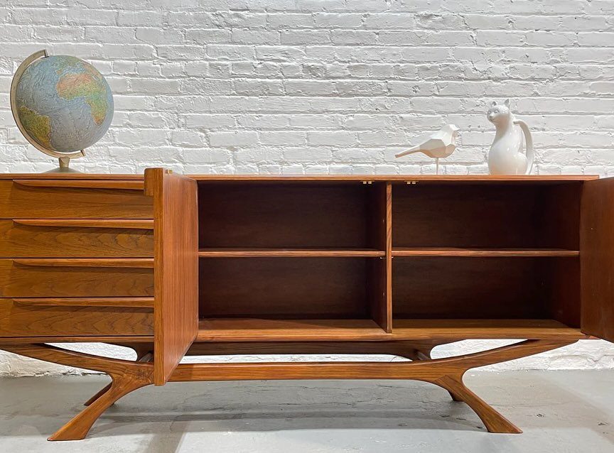 Mid-century modern wooden sideboard with a globe and bird figurines against brick wall