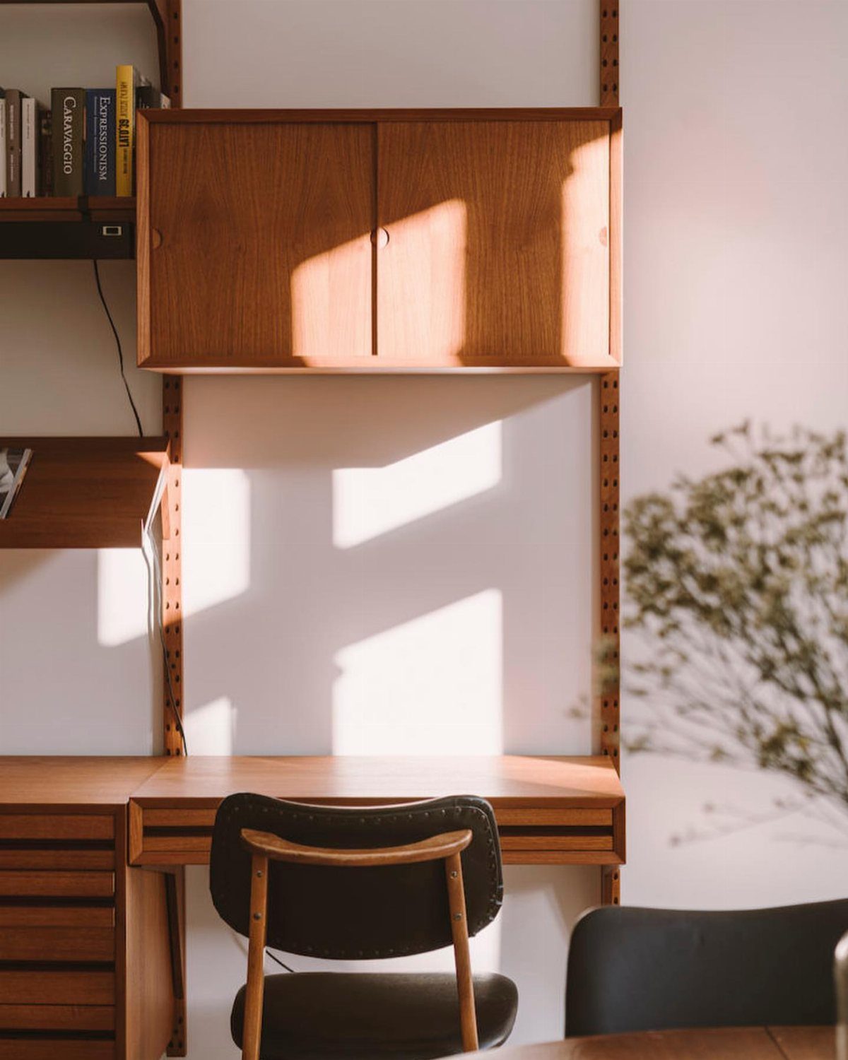Mid century modern wooden desk and wall cabinet with a black office chair.