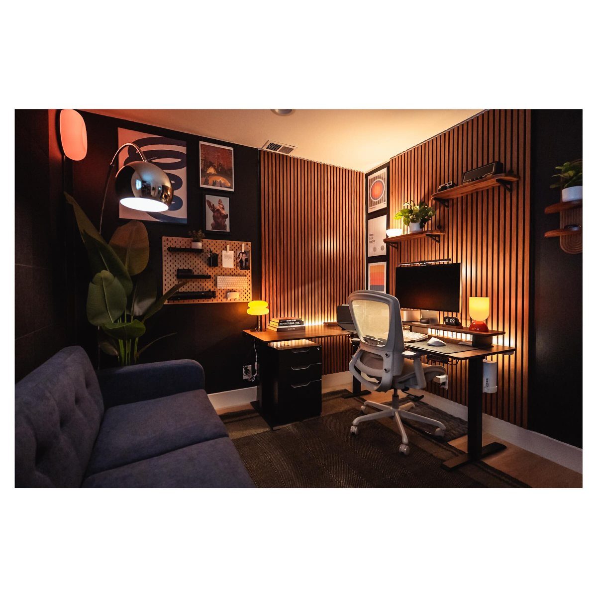 Modern home office with wooden slat wall, ergonomic chair, and blue sofa.