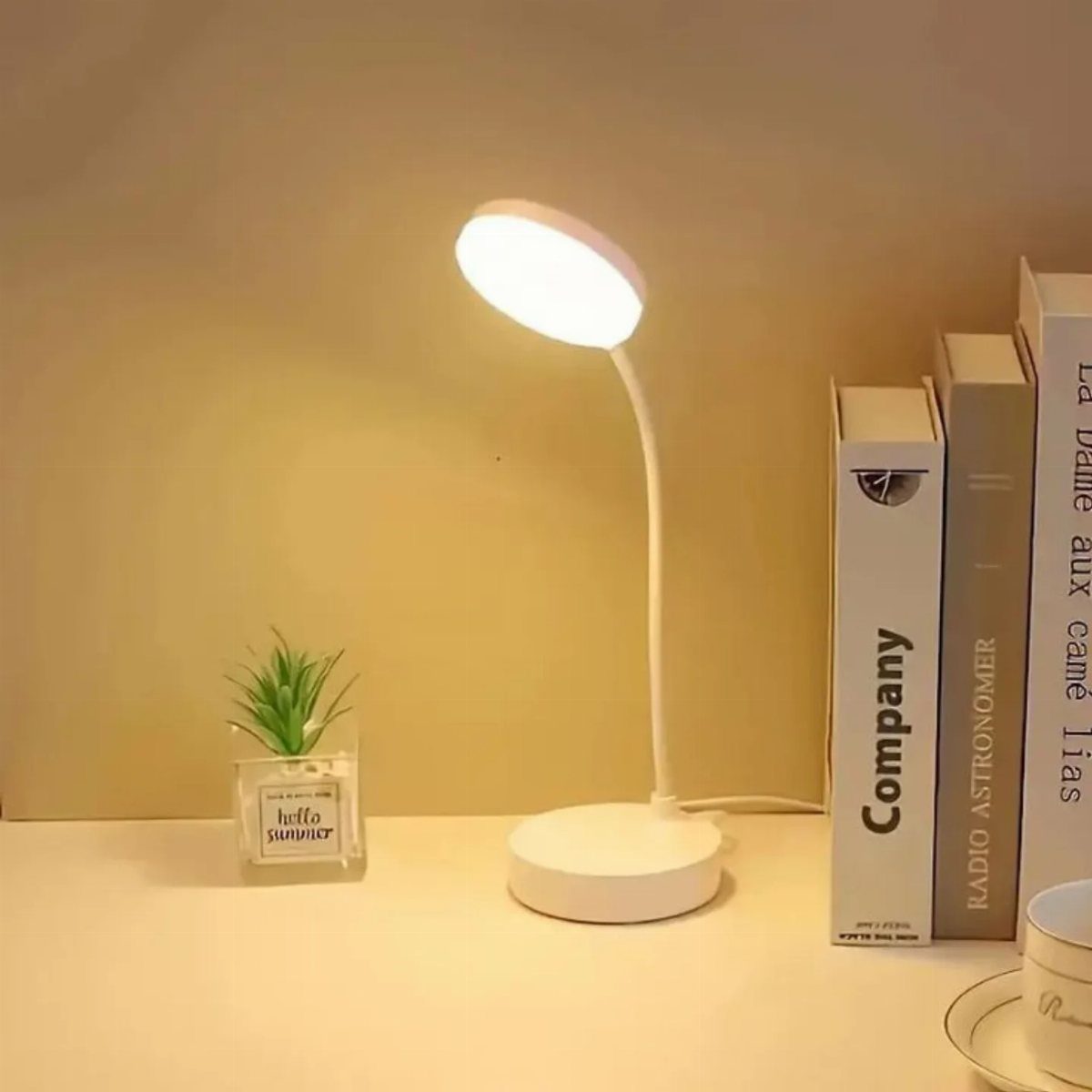 White modern desk lamp lighting a white desk with books and a plant.