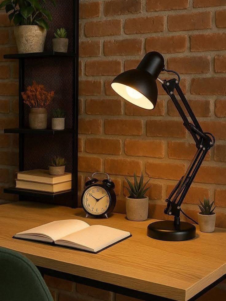 Wooden desk with black lamp, open notebook, and alarm clock against brick wall