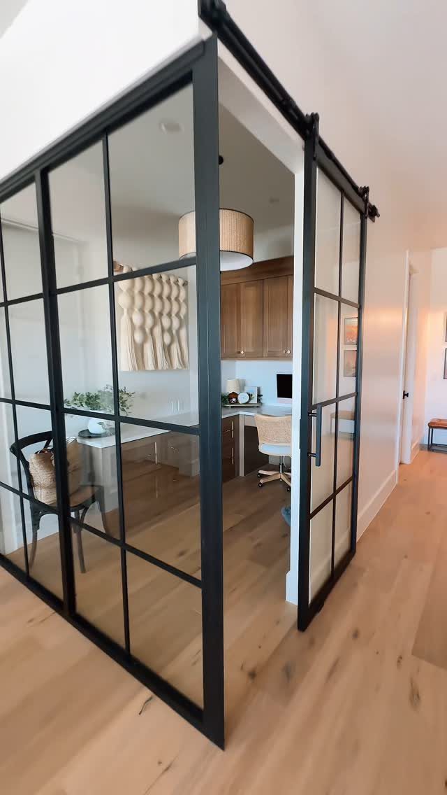 Black-framed glass sliding doors opening into a modern home office with wooden furniture.