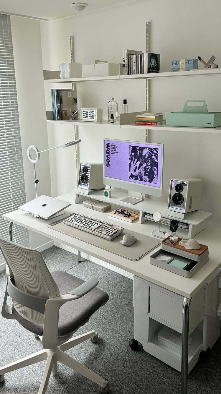 White home office desk with a computer, ergonomic chair, and small white speakers.