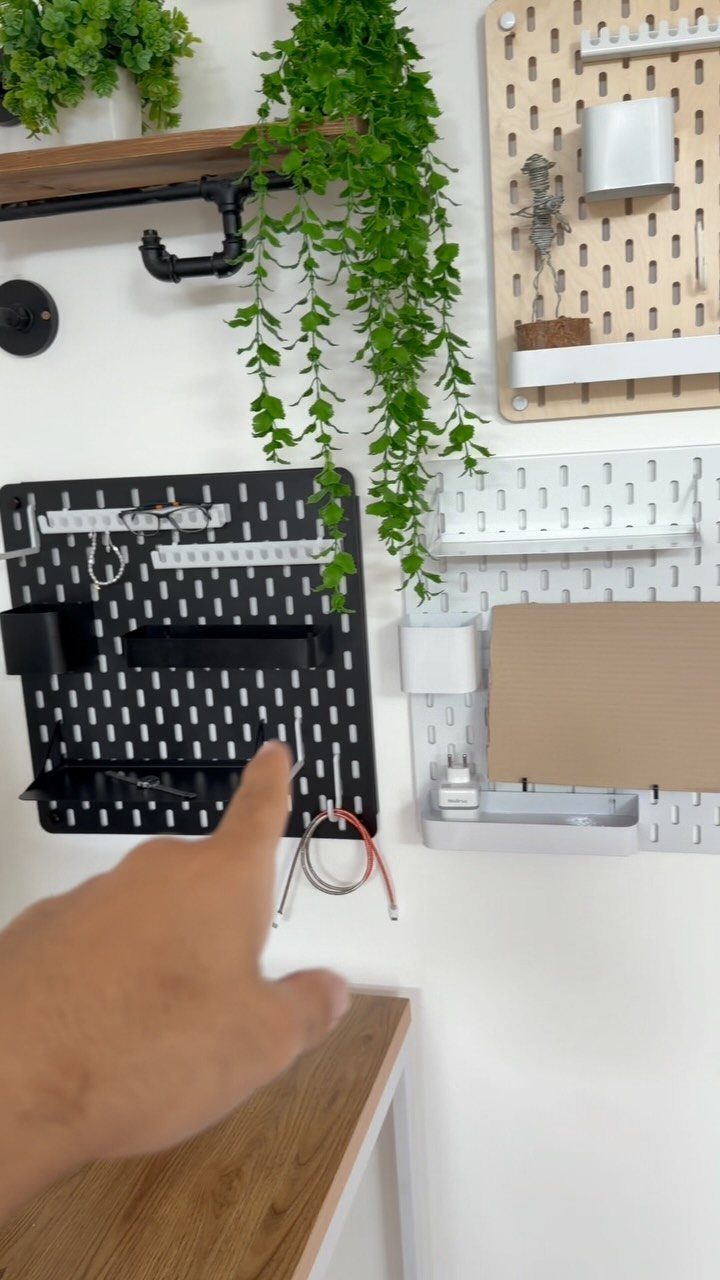 Black and white pegboards on a white wall with trailing green plants above.