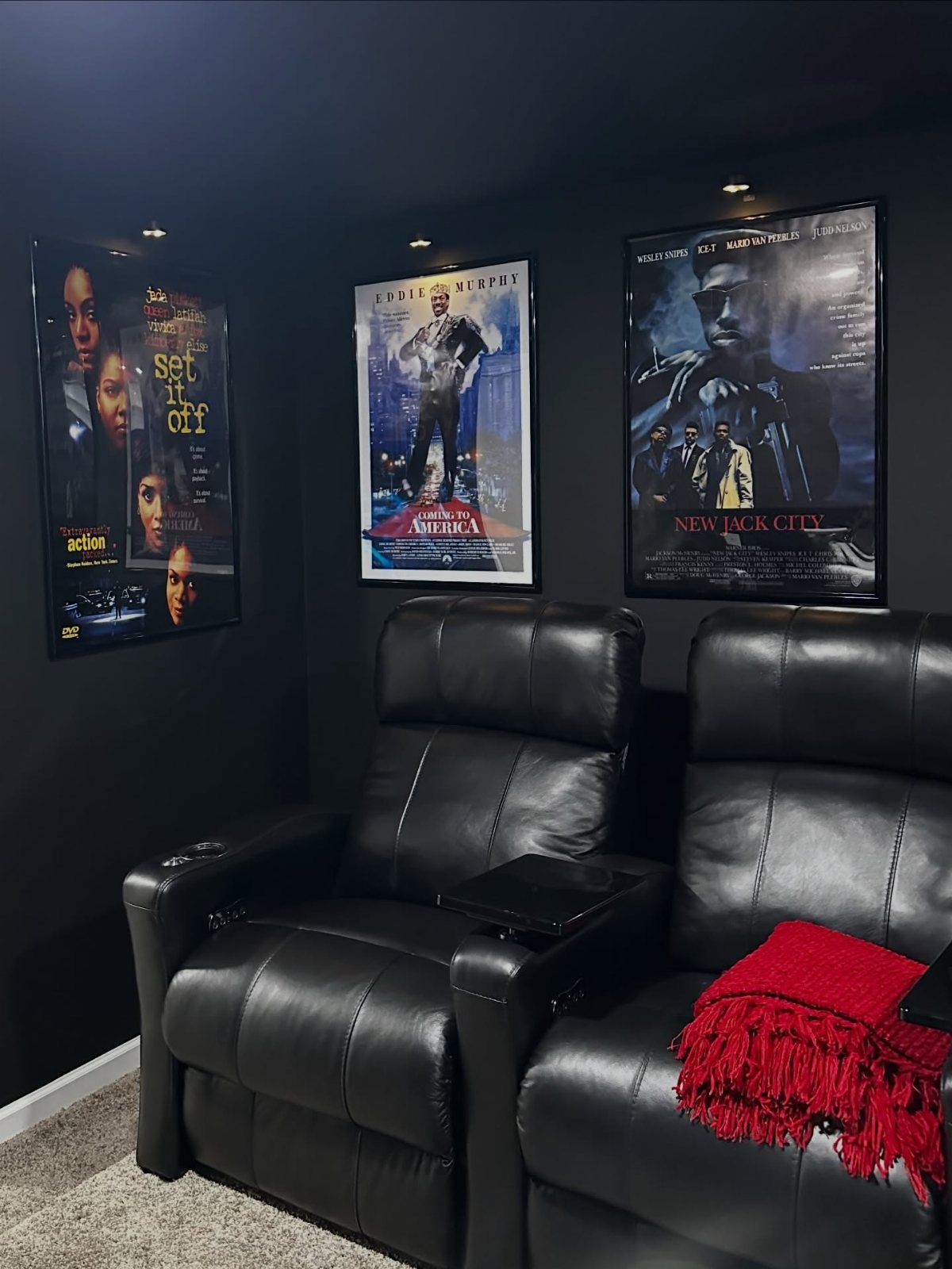 Black leather recliners in a home theater with matte black walls and movie posters.