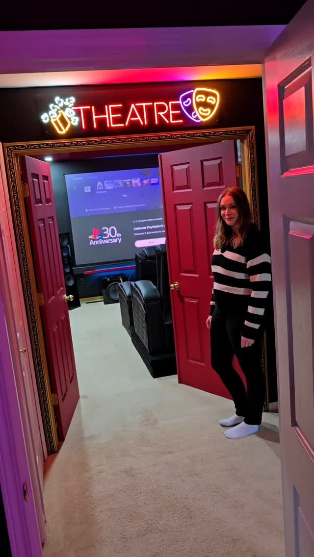 Woman standing in a doorway of a home theater with neon signage and screen.