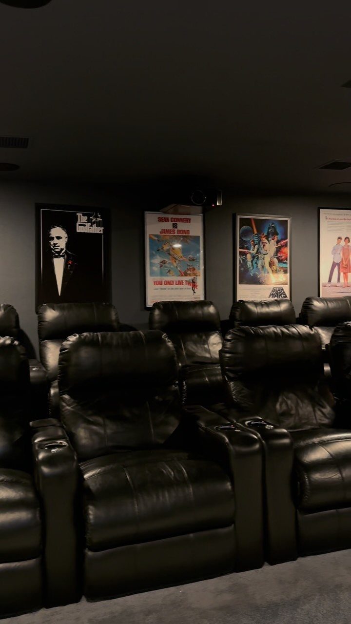 Black leather reclining theater seats in a dark home cinema with movie posters.