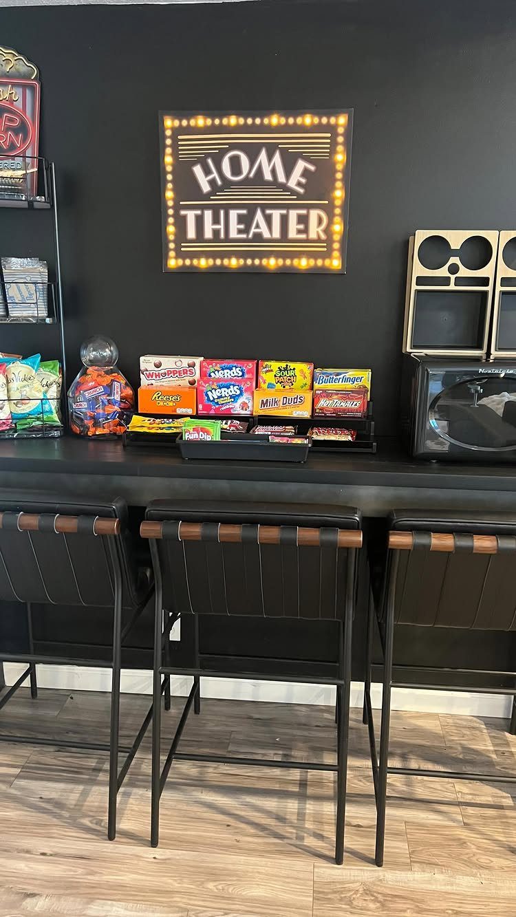 Home theater snack bar with colorful candies on a black counter and bar stools.