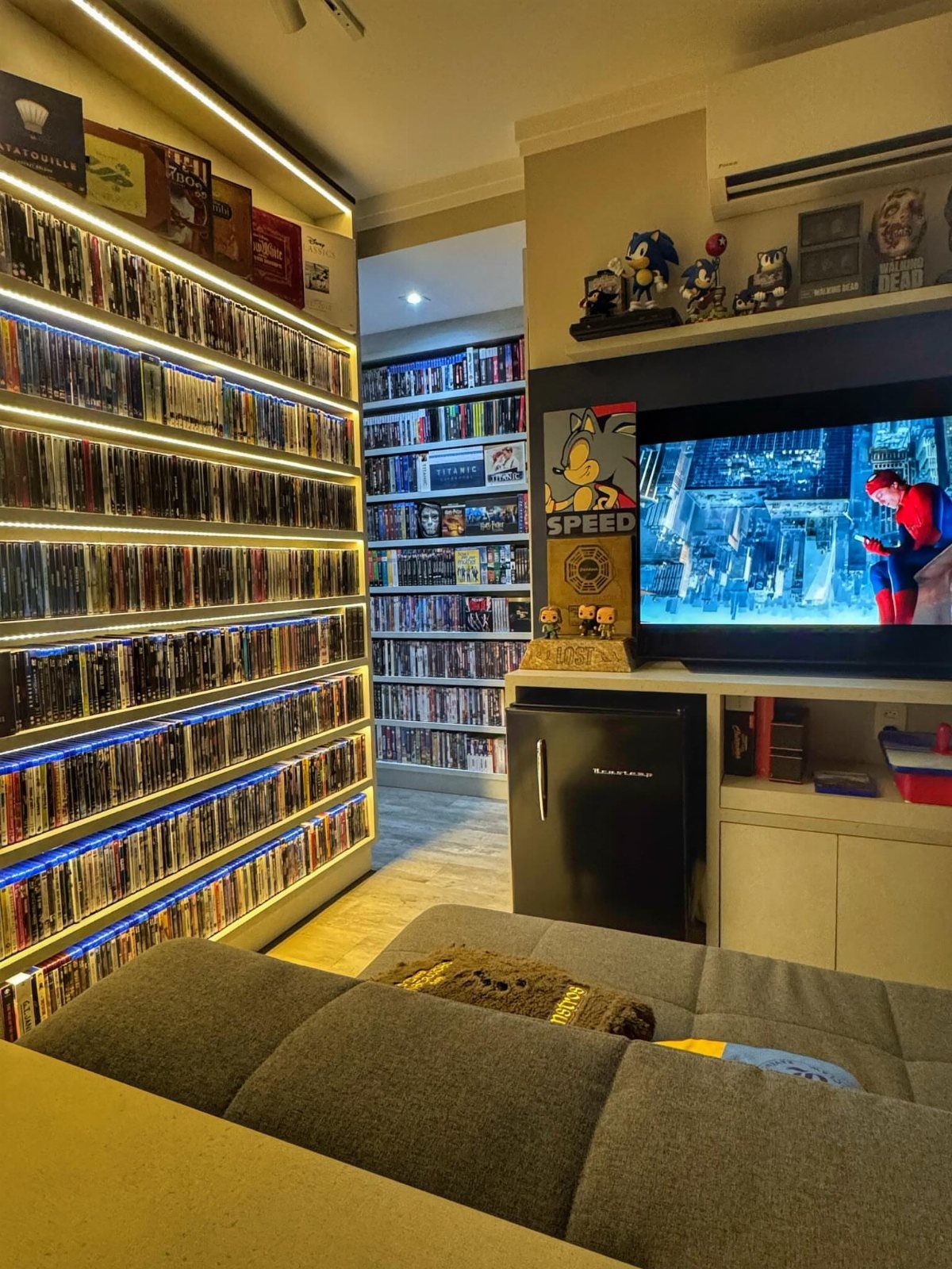 Built-in illuminated shelving units filled with movies in a home theater room.