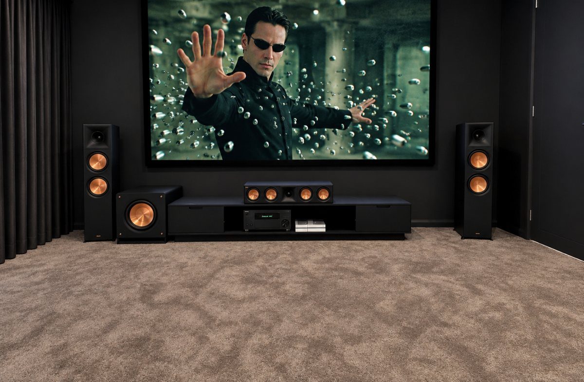 Home theater system with large screen, black speakers, and brown carpeted floor.
