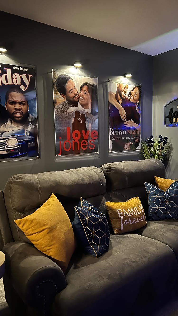 Framed movie posters on a dark wall above a grey sofa with pillows.