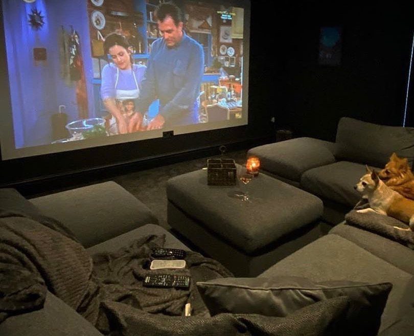 Dark home cinema room with a large projection screen and grey sectional sofas.