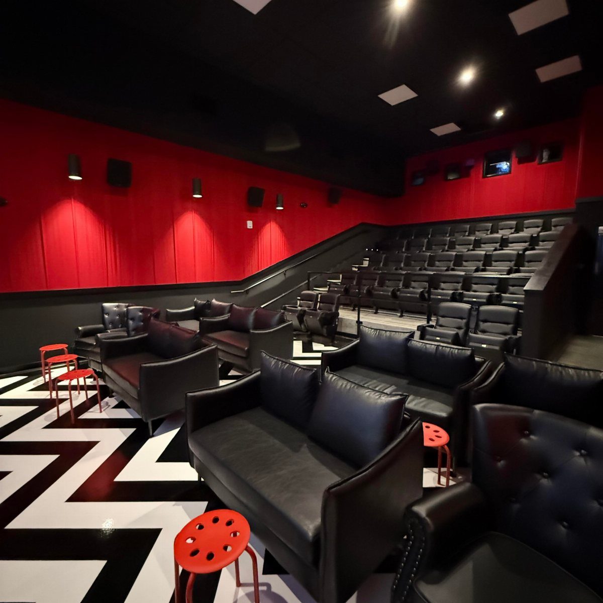 Movie theater room with red walls, black leather seating, and geometric patterned flooring.
