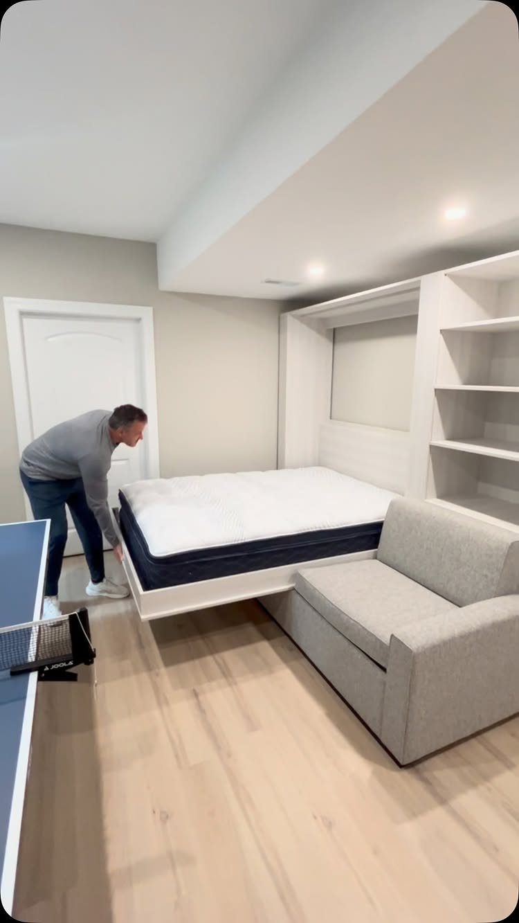 Man pulling down a white murphy bed in a room with a sofa.