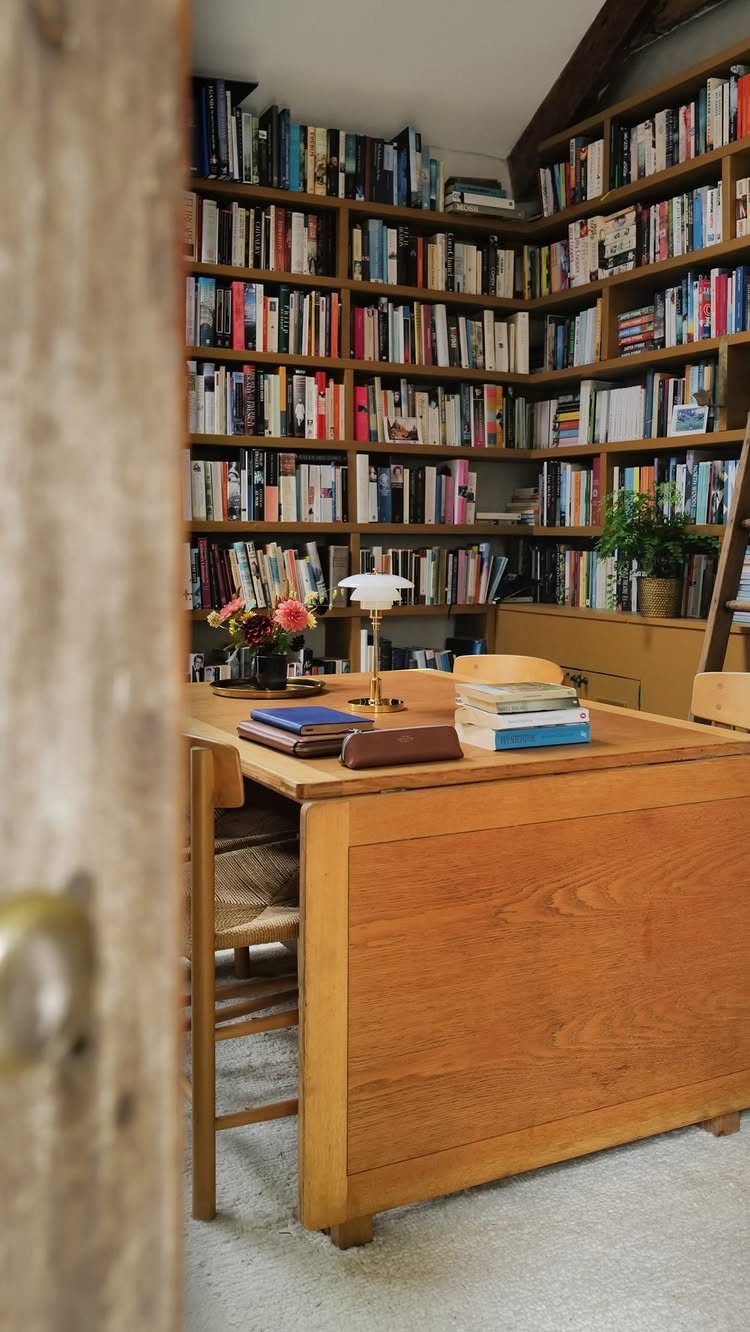 Wooden desk and floor-to-ceiling bookshelves filled with books in a home office.